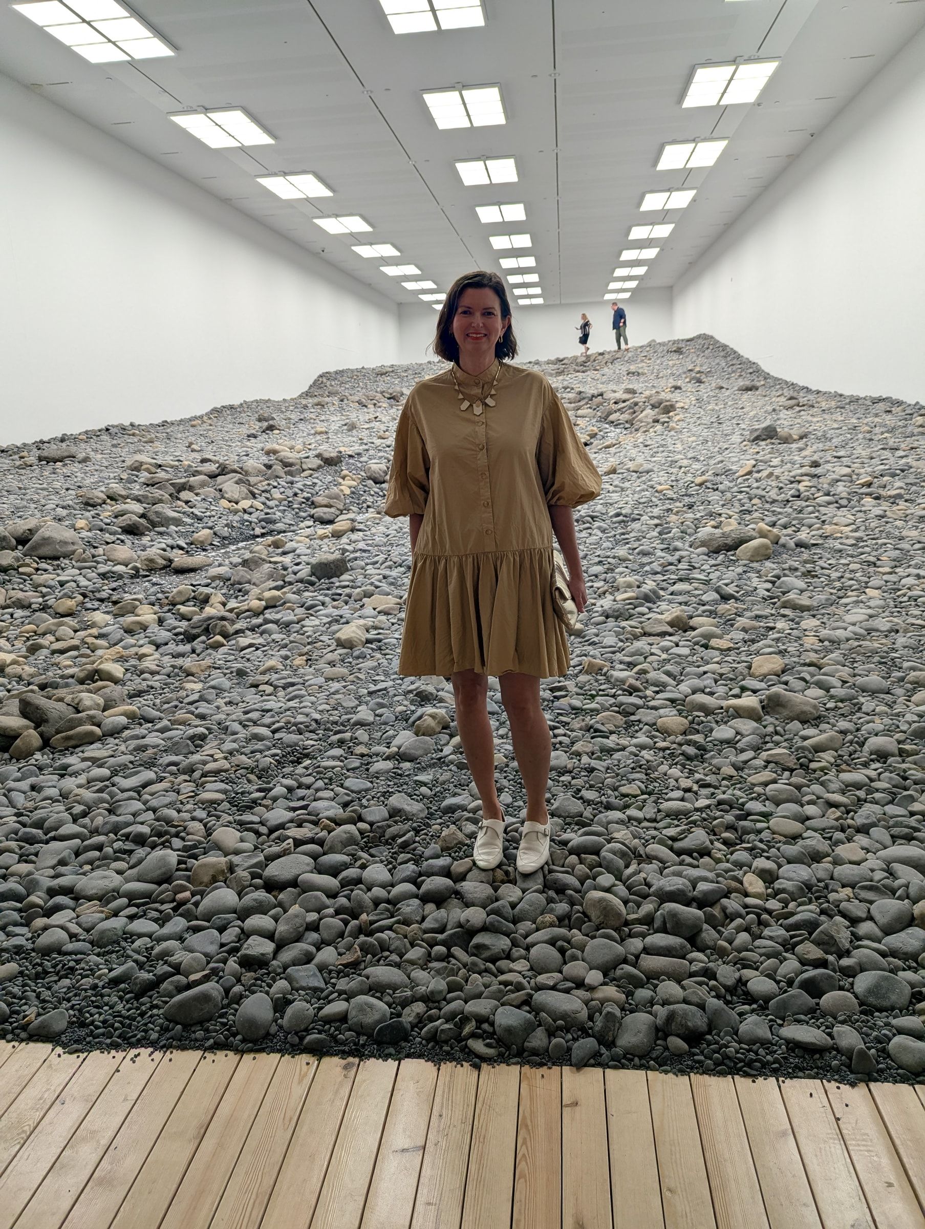 Megan Franks standing on the Riverbed rocks in a long white gallery, ceiling lights receding behind her.