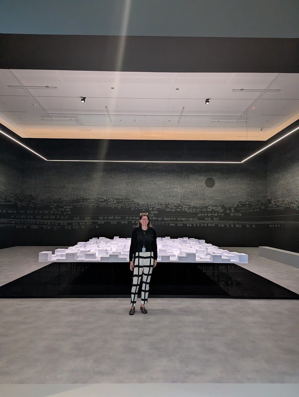 Megan Franks standing in the kith and kin gallery: chalk genealogy across the black walls and the central table of stacked documents behind her.
